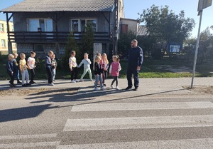 policjant stoi z dziecmi przy przejściu dla pieszych