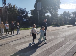 policjant i dwoje dzieci przechodzi przez przejście dla pieszych