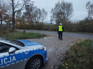 policjant stoi przy drodze, za nim stoi radiowóz