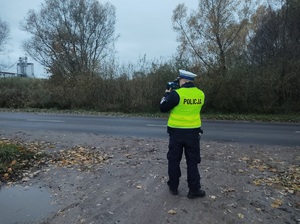 policjant stoi przy drodze i mierzy predkość urzadzeniem