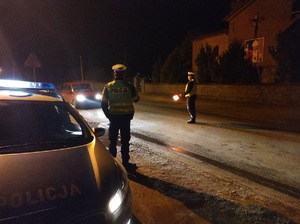 policjanci stoja na drodze, jeden z nich latarką zatrzymuje samochód